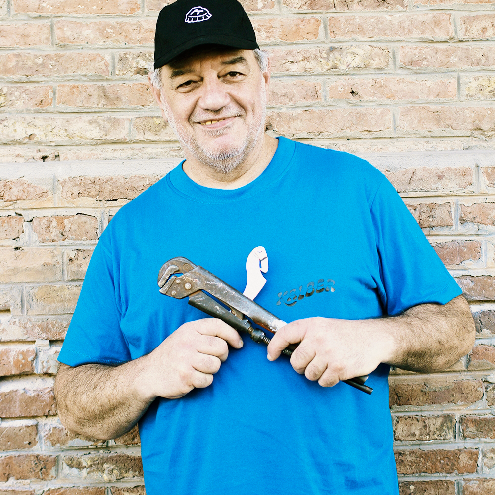 Señor con gorra negra y remera azul con marca de la empresa, en sus manos tiene dos herramientas cruzadas