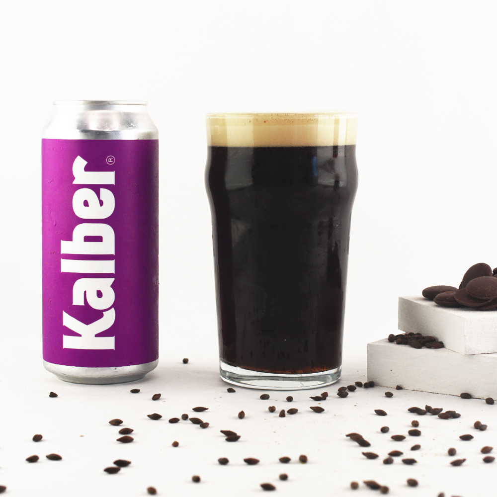 cerveza sweet stout en vaso, lata violeta al lado, malta y chocolaste esparcida