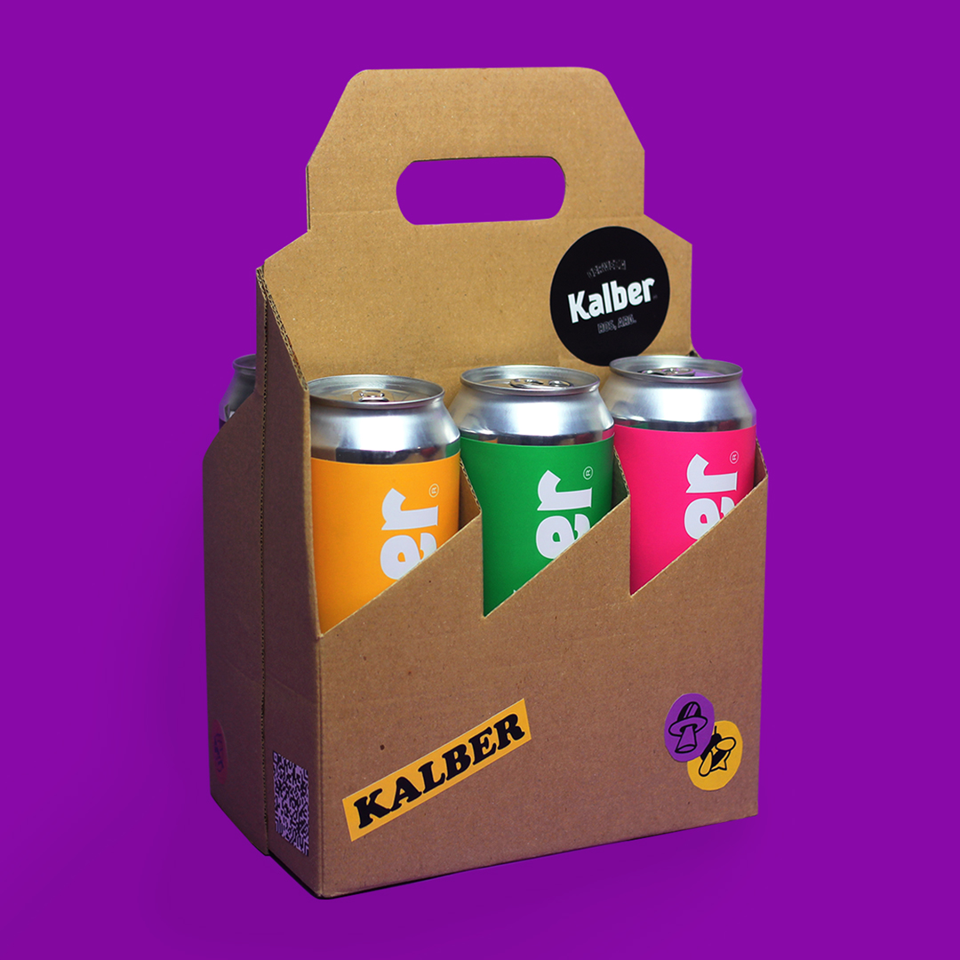 Pack de 6 birras, se ven 3 latas de colores variados en un pack de color madera con stickers de la marca